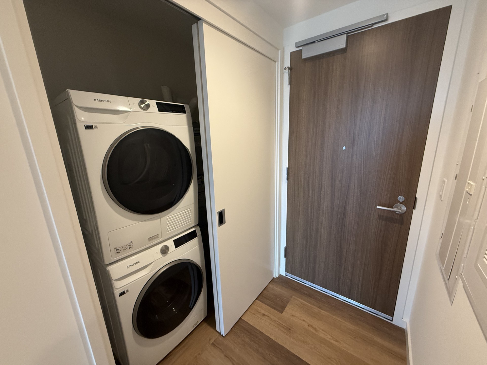 A white dryer is in a small closet next to a brown door.